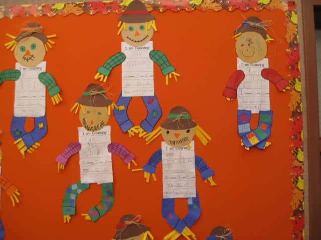 Student-made place value scarecrows displayed on an orange fall bulletin board.